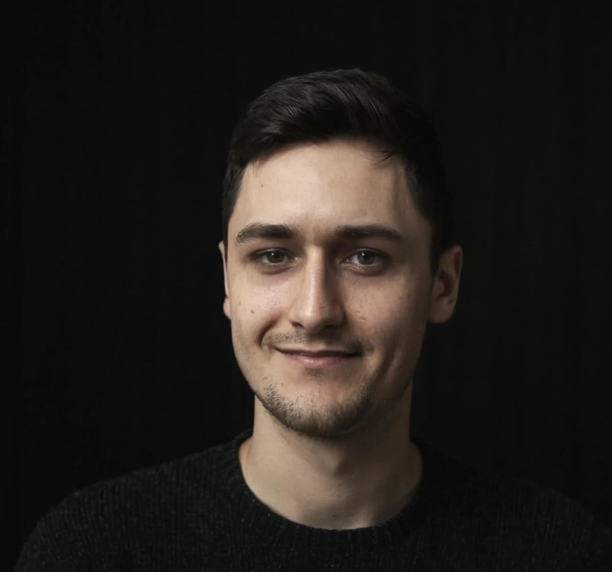 Adam Noszczyński Zdjęcie przedstawia portret Adama Noszczyńskiego w czarnym swetrze i na czarnym tle